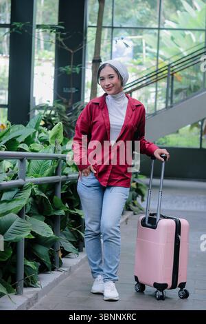 Una giovane donna che indossa un hijab, in piedi con i suoi bagagli, è pronta per un'avventura o una fuga emozionante. Cattura l'essenza dell'esplorazione in solitaria, h Foto Stock