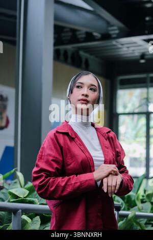 Una giovane donna che indossa un hijab si erge graziosamente in un giardino botanico, il suo sguardo pensivo trasmette un senso di serenità e una meditazione ponderata ben Foto Stock