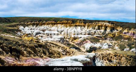 Una vibrante scogliera gialla domina il primo piano, mentre le formazioni di arenaria pastello delle miniere dipinte si estendono dietro di esso. Foto Stock