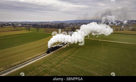Una veduta aerea di un treno passeggeri a vapore che si avvicina, viaggiando attraverso le Farmlands aperte, soffiando un sacco di fumo bianco, in un giorno d'inverno Foto Stock