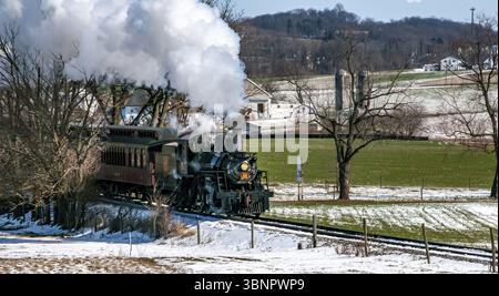 Ronks, Pennsylvania, Stati Uniti, 17 febbraio 2024 - Un treno a vapore sta attraversando un campo innevato. Il treno a vapore è bianco e nero ed è circondato Foto Stock
