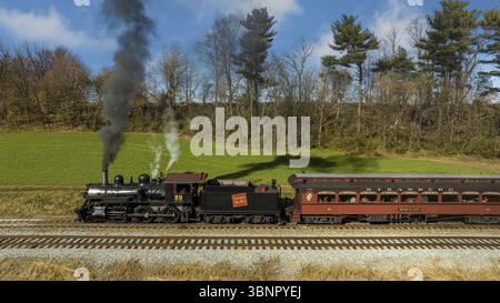 Ronks, Pennsylvania, 26 novembre 2022 - Vista di un drone su un treno passeggeri a vapore restaurato che viaggia attraverso le fattorie che si dirigono verso una piccola stazione su un An Foto Stock