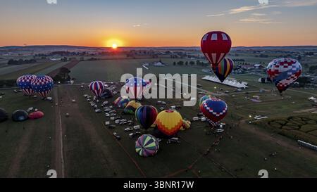 Una dozzina di colorate mongolfiere si stanno preparando per il lancio in un campo di festival durante il tramonto. Gli spettatori si riuniscono per assistere allo spettacolo come la sera Foto Stock