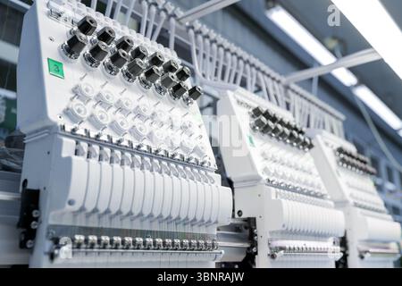 Primo piano di una macchina da ricamo avanzata che lavora su tessuti, mostrando il processo di cucito industriale e la produzione tessile Foto Stock