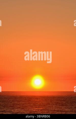 La fine è vicina, un tramonto dorato-arancione con il sole che raggiunge la linea dell'orizzonte che annuncia che la notte sta cadendo Foto Stock