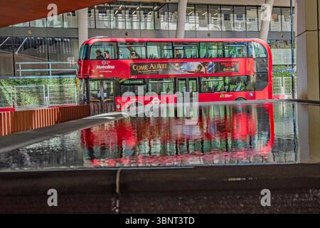 Un London Bright Red Bus catturato riflesso in un London Street Water Feature Foto Stock