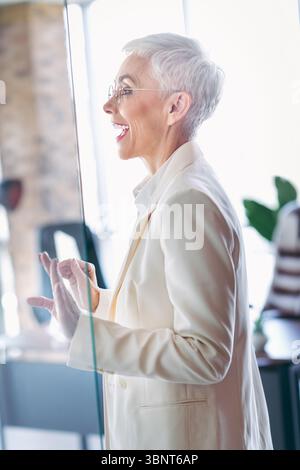 Elegante donna d'affari anziana impegnata in discussioni in ufficio, mostrando il comportamento professionale e la fiducia personale Foto Stock