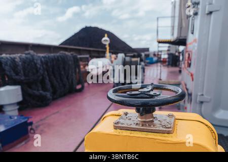 Una nave portarinfuse è attraccata in un porto affollato, impegnata nel processo di carico del carbone. Il primo piano è dotato di un grande controllo del distributore giallo, che suggerisce Foto Stock