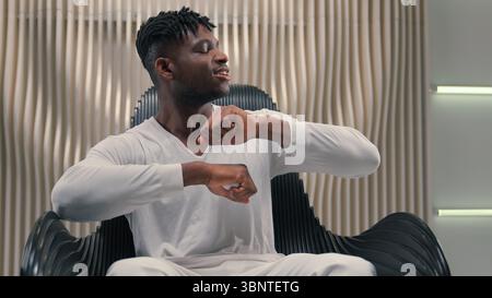 Ragazzo afroamericano uomo etnico maschio ascoltare musica in cuffie ballare braccia ondulate ballare ascoltare canzone in auricolari wireless seduti in futuristico Foto Stock
