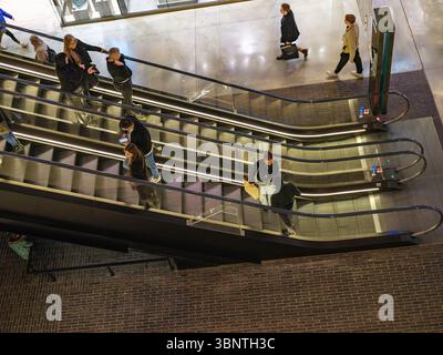 Londra, Regno Unito, 16 dicembre 2024. Gli amanti dello shopping fanno un giro sulle scale mobili in un affollato centro commerciale nel centro di Londra, visto dall'alto in bianco e nero. Foto Stock
