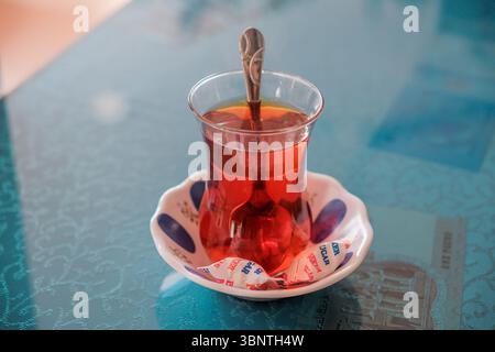 Bicchiere di tè turco sul tavolo, tradizionale tè nero Cay, bevanda calda ambra in vetro a forma di tulipano, dettaglio della cultura del tè, scena di ospitalità quotidiana Foto Stock