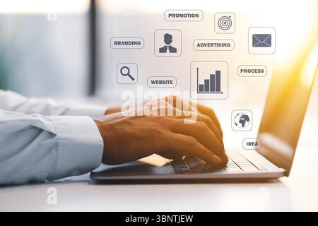 Marketing digitale. Uomo d'affari che usa un portatile a tavola, primo piano. Icone e parole sullo schermo virtuale Foto Stock