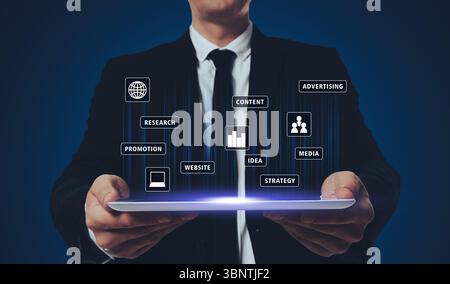 Marketing digitale. Uomo d'affari che tiene un tablet su sfondo scuro, primo piano. Icone e parole sopra il dispositivo Foto Stock