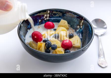 Una persona che versa il latte in una ciotola di muesli fatti in casa isolata su sfondo bianco. Foto Stock