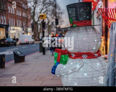 Regno Unito, Londra, 11 dicembre 2024. Un pupazzo di neve illuminato festoso si erge fuori da un negozio in un quartiere di Londra, aggiungendo il tifo stagionale al Foto Stock