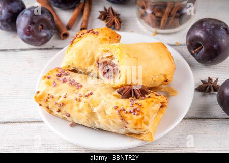 Vertuta, torte fatte in casa con marmellata di prugne dolci e ripieno piccante, con cannella, su uno sfondo di cucina in legno con succose prugne scure e spi Foto Stock