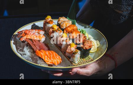 Piatto di sushi assortito con sashimi freschi e nigiri tenuto a mano da una donna. Foto Stock
