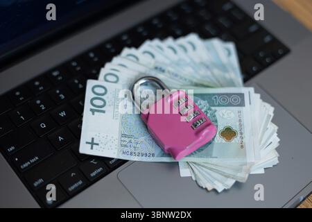 Sicurezza finanziaria nell'era di Internet. Una pila di 100 note Zloty protette con Un lucchetto rosa su Una tastiera di un notebook. Simbolo di sicurezza online banking e EN Foto Stock