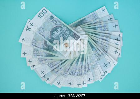 Pila di 100 banconote in zloty polacche disposte a forma di ventaglio su sfondo blu. Concetto di ricchezza, cassa, Finanza, valuta o risparmio Foto Stock