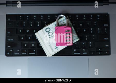 Una pila di banconote Zloty polacche assicurate con Un lucchetto a combinazione rosa su Una tastiera per laptop. Concetto di sicurezza informatica, sicurezza bancaria online, Financ Foto Stock