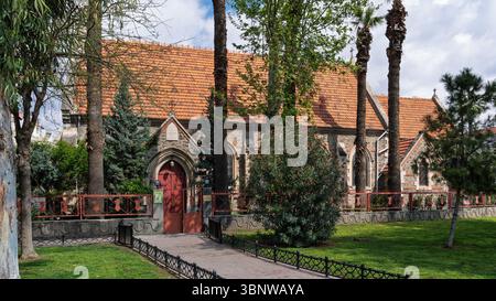 Chiesa di San Giovanni Evangelista, Smirne, Turchia. Esterno della storica chiesa anglicana con tetto rosso, pareti in pietra, giardino e alberi, in una giornata di sole Foto Stock