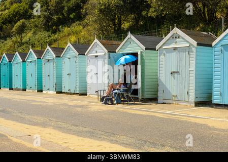 Bournemouth, Dorset, Inghilterra, Regno Unito, venerdì 4 luglio 2025, Meteo: Persone in una capanna sulla spiaggia con caldo sole pomeridiano estivo sulla costa meridionale prima di passare al tempo piovoso durante il fine settimana. Foto Stock