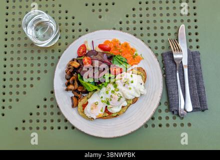 Piatto da buongustai con uova in camicia, pane tostato all'avocado, salmone affumicato e insalata fresca. Vista dall'alto. Brunch sano ed equilibrato con toast all'avocado Foto Stock