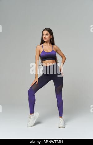 Una donna atletica indossa con sicurezza l'elegante abbigliamento sportivo viola, con top e leggings, abbinati a sneaker bianche. Capelli lunghi e concentrati Foto Stock
