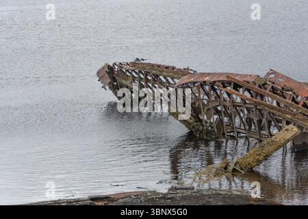 Scheletri arrugginiti di vecchie navi in legno parzialmente sommersi in acque calme, creando una scena drammatica e malinconica di decadimento e storia Foto Stock