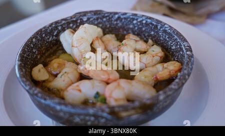 Piatto di gamberi servito in una ciotola rustica in un ristorante mediterraneo, con un delizioso pasto a base di pesce al coperto su un tavolo con aglio e una forchetta per di Foto Stock