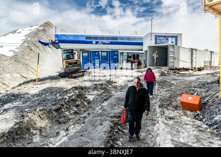 Titlis 3020, importante cantiere edile. Si prevede che fino al 2029 sarà il più grande cantiere delle Alpi, con gru da costruzione, escavatori e betoniere. Il principale progetto "Titlis 3020" prevede la costruzione di una nuova stazione a monte a un'altitudine di 3.020 metri e l'ampliamento di una nuova funivia e negozi per l'acquisto di beni di lusso. I visitatori camminano lungo un sentiero roccioso e innevato nel paesaggio alpino di Engelberg, Obwalden, Svizzera. La stazione della funivia Ice Flyer può essere vista sullo sfondo, circondata da edifici temporanei e tappeto da cantiere Foto Stock