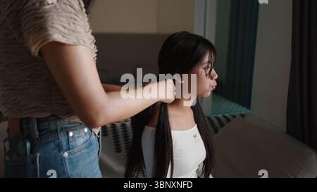 Donna che intreccia i capelli di un'altra donna al chiuso in una camera da letto Foto Stock