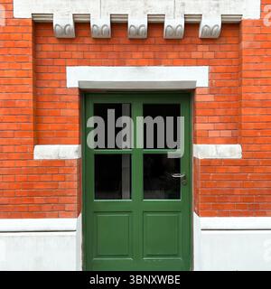 Una porta con pannelli verdi e moderni vetri si apre sul cortile di Hala Koszyki a Varsavia, incorniciato da mattoni rossi restaurati e dettagli bianchi Foto Stock