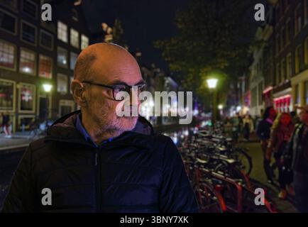 Un uomo contemplativo cammina lungo una vivace strada della città di notte, circondato da luci luminose, architettura storica e un'atmosfera vivace di persone Foto Stock