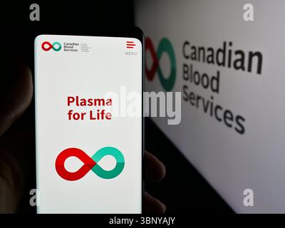 In questa illustrazione fotografica, una persona sta tenendo un cellulare con la pagina web dell'organizzazione sanitaria Canadian Blood Services sullo schermo davanti al logo. Foto Stock