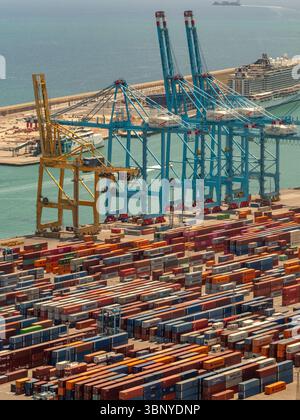 Le gru a cavalletto si trovano su pile di container nel porto di Barcellona, con una nave da crociera visibile sullo sfondo, la Spagna. Foto Stock