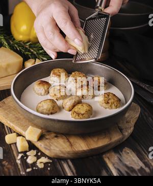 Cibo natura morta, donna che grattugia il parmigiano sulle polpette in salsa panna Foto Stock