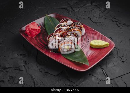 Natura morta del cibo, sushi roll assortiti sono presentati artisticamente su un piatto rosso, accentuato da zenzero sottaceto e wasabi, che mostrano il testo delicato Foto Stock
