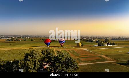 Alla luce del mattino presto, le vivaci mongolfiere sono pronte per la salita tra ampi campi e un'idilliaca vista sulla campagna. L'atmosfera calma Foto Stock