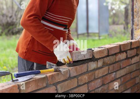 Un uomo costruisce un muro di mattoni, mette un mattone su una Malta di cemento-sabbia Foto Stock