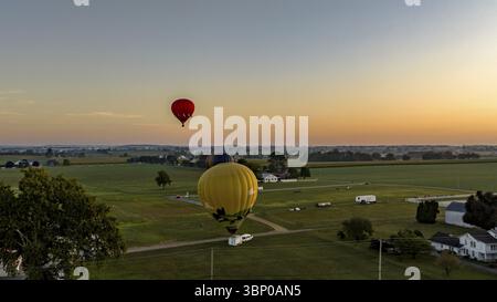 Una vista aerea di tre mongolfiere che si preparano per il lancio, con una in aria, galleggiante, in un lancio mattutino, in un giorno estivo Foto Stock