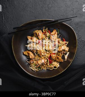 Natura morta degli alimenti, mescolare gli spaghetti con verdure e pollo in un recipiente nero Foto Stock