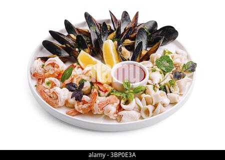 Natura morta del cibo, Un vivace piatto di pesce espone gamberi freschi, cozze e calamari disposti splendidamente con spicchi di limone e una ricca salsa. Foto Stock