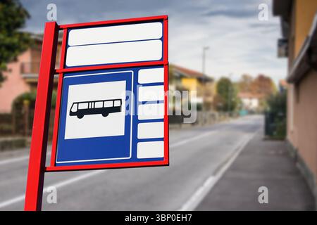 La fermata dell'autobus si trova sulla strada vuota. Elemento delle infrastrutture urbane con telaio rosso. Marciapiede e case sullo sfondo. Trasporto pubblico per piccole città. Foto Stock