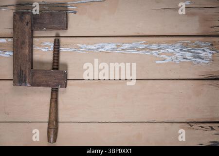 Morsetto in legno molto vecchio posto sul bordo sinistro di un tavolo in legno beige usurato. Il resto della cornice lascia molto spazio vuoto per il testo o la progettazione. Foto Stock