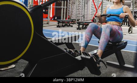 Movimento: Vestibilità e concentrazione di una giovane donna in abbigliamento sportivo che si allena su una macchina da canottaggio durante una sessione di allenamento da sola in palestra. Foto Stock