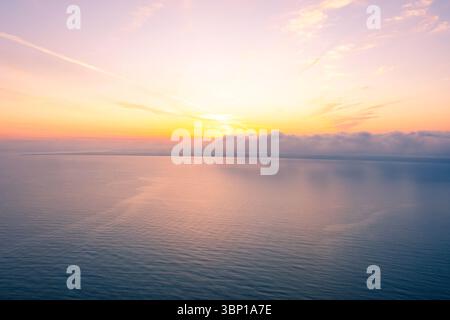 Vista aerea del tramonto dorato sull'oceano calmo con lo strato di nebbia che si estende su Horizon Foto Stock