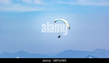 Un parapendio tandem vola in aria, mostrando un paracadute luminoso e colorato sullo sfondo delle montagne bavaresi. Foto Stock