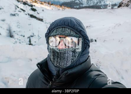 Un uomo che indossa una giacca nera e una sciarpa con una macchina fotografica in mano. Sta indossando occhiali da sole e un cappello Foto Stock