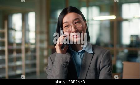 Donna d'affari asiatica sorridente parlare telefono cellulare donna cinese imprenditore manager architetto ingegnere parlare chiamata comunicazione smartphone Foto Stock